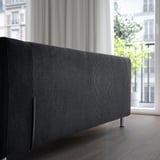 Dark sofa near large window. Soft fabric cover, removable for cleaning. Modern, comfortable design with metal springs.