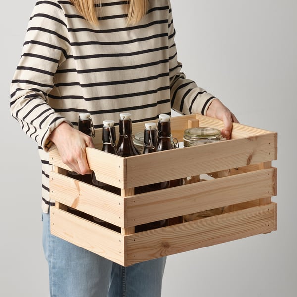 A woman holding a wooden crate with bottles. The crate has handles for easy lifting.