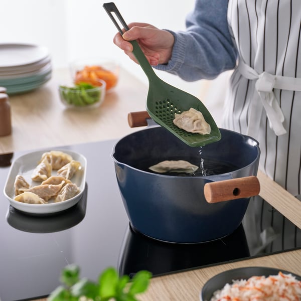 A person lifts boiled dumplings using a green KNORRHANE utensil, showcasing its lifting function.