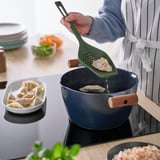 A person lifts boiled dumplings using a green KNORRHANE utensil, showcasing its lifting function.