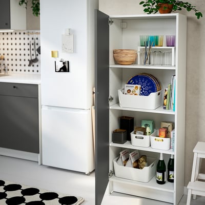 Kitchen cabinet with open door displaying storage boxes, dishes, and wine bottles.