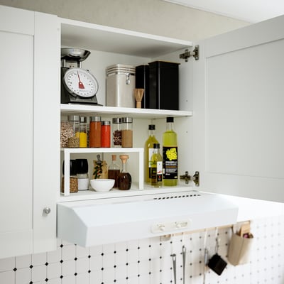 White wall cabinet with adjustable shelves, holding kitchen items like bottles, jars, and a food scale, mounted on a tiled wall.