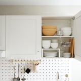Kitchen cabinet with wooden bowls, plates, and metal utensils stored.