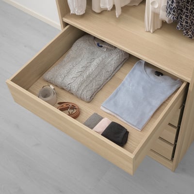 Open wooden drawer showing folded sweater, shirt, socks, and accessories, demonstrating organized storage in a wardrobe.