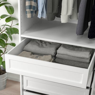 White pax drawer open, neatly folded gray clothes inside. Plant on wooden floor beside.