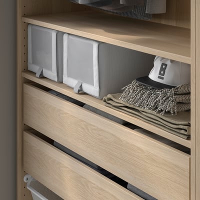 A wooden closet interior with light-colored KOMPLEMENT shelves. One shelf holds gray textured skubb boxes and folded clothes.
