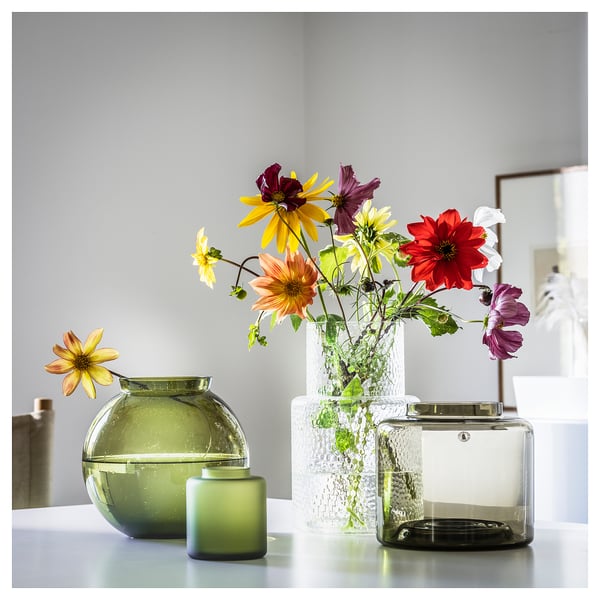 KONSTFULL green glass vases, round and tall, holding colorful flowers, sitting on a white table.