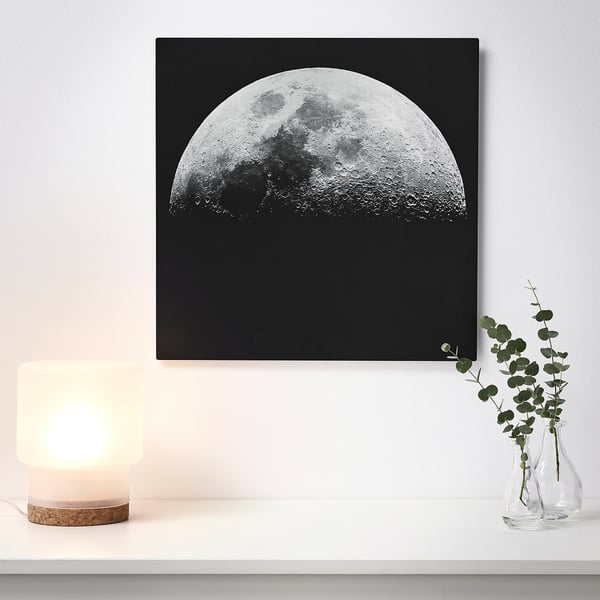 A wall art of a half moon on a black background, illuminated by a nearby lamp, giving a 3d effect.