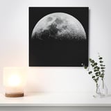 A wall art of a half moon on a black background, illuminated by a nearby lamp, giving a 3d effect.