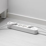 White multi-socket with usb ports on a wooden floor. Two cables plugged in, one with a white connector.