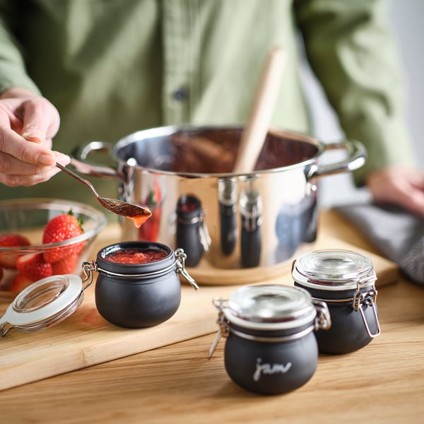 Person pours jam into KORKEN jars on a wooden table, preserving it for storage.