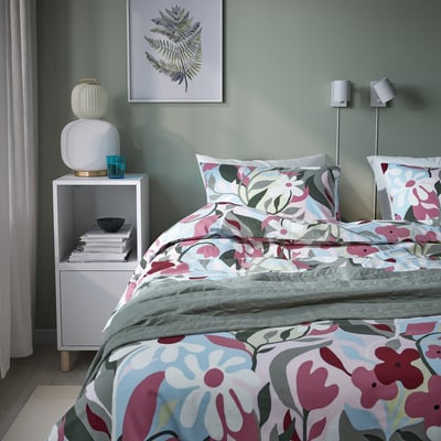 Cozy bedroom with KORSKOVALL floral bedding, green wall, leaf print, modern lamps, white nightstand & turquoise glass.
