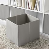 Empty gray folding storage box next to bookshelf on carpeted floor.