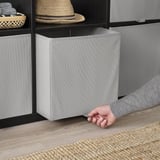 Person reaching into KOSINGEN storage box on shelf. Easy to assemble and fold, perfect for organizing bulky items.