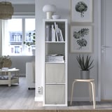 Stylish living room with white KOSINGEN storage box, gray plant, art prints, light wood stool.