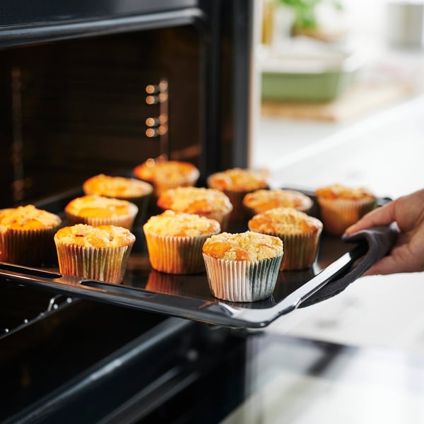 Hand holding tray of golden muffins in colorful liners being removed from oven.