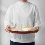 Person holding a bamboo serving tray with two glasses and books, perfect for serving or carrying items.