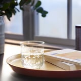 A round bamboo tray holds an embossed glass cup, ideal for serving drinks and carrying items.