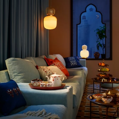 Cozy living room with blue sofa, colorful pillows, hanging lamp, and bamboo tray with tea set.