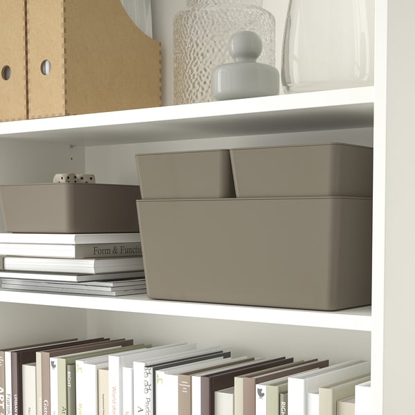 A white bookshelf displays KUGGIS storage boxes and books. The boxes organize small items, with one stackable lid-optional.