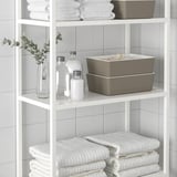 White shelves with organized items: towels, bottles, box, and plant.