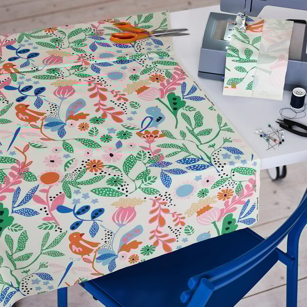Colorful, patterned fabric displayed on a blue chair, ideal for sewing projects, with scissors, thread, and a sewing machine shown nearby.