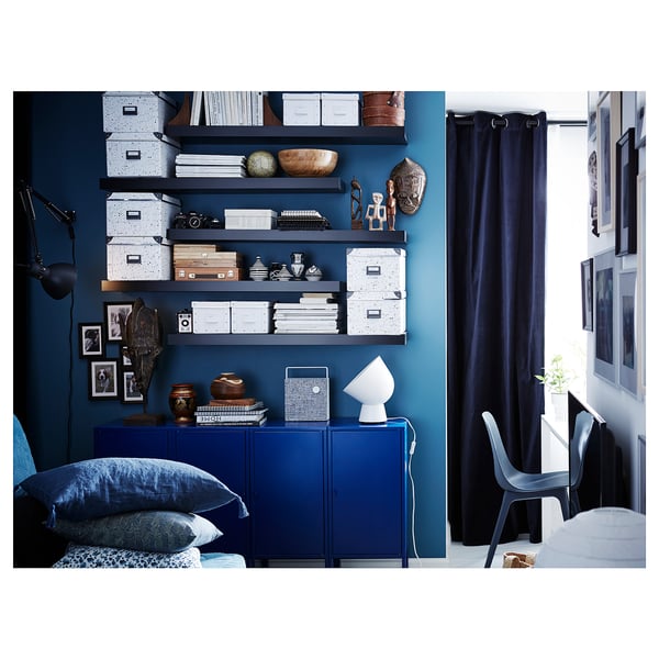 Modern blue room with blue wall, LACK shelves with various items, blue cabinet, blue curtains, and minimalist furniture.