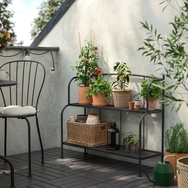 Black LÄCKÖ plant shelf holds potted herbs & plants, fits balcony with chair.
