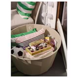 Large white storage bin filled with colorful items, placed in a cozy room with a striped pillow.
