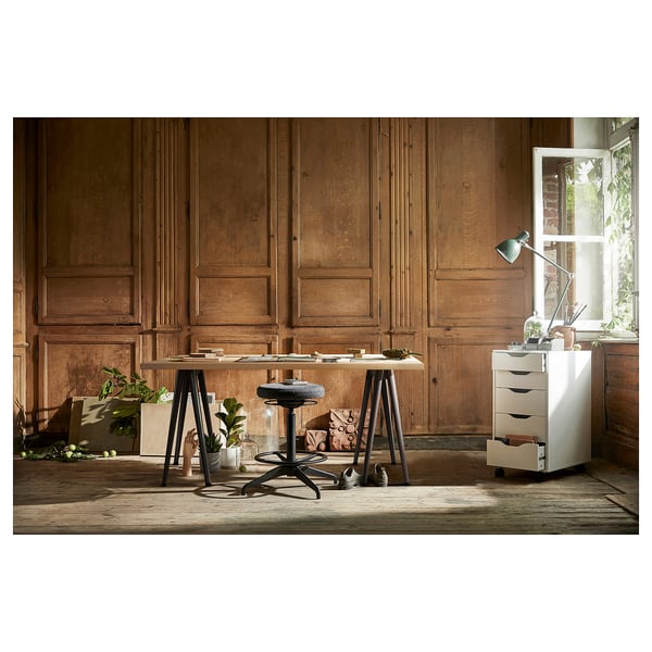 Home office: wooden walls, white desk, grey stool, drawer, plants, lamp.