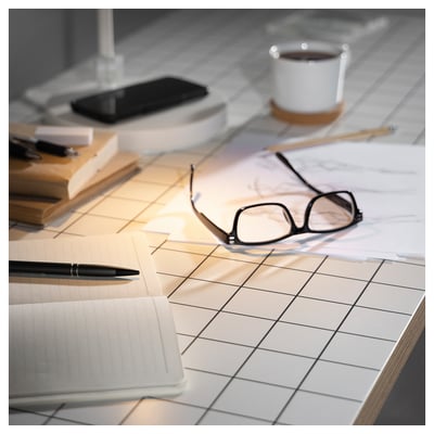 A white LAGKAPTEN tabletop with square pattern, made from fibreboard and paper filling, glasses, a pen, and a cup.