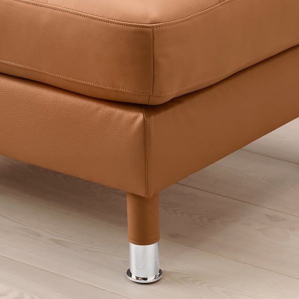 Close-up of a brown leather footstool on a wooden floor, showcasing its sturdy chrome legs and high-quality upholstery.