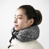 Woman with updo and light top using adjustable travel neck pillow.