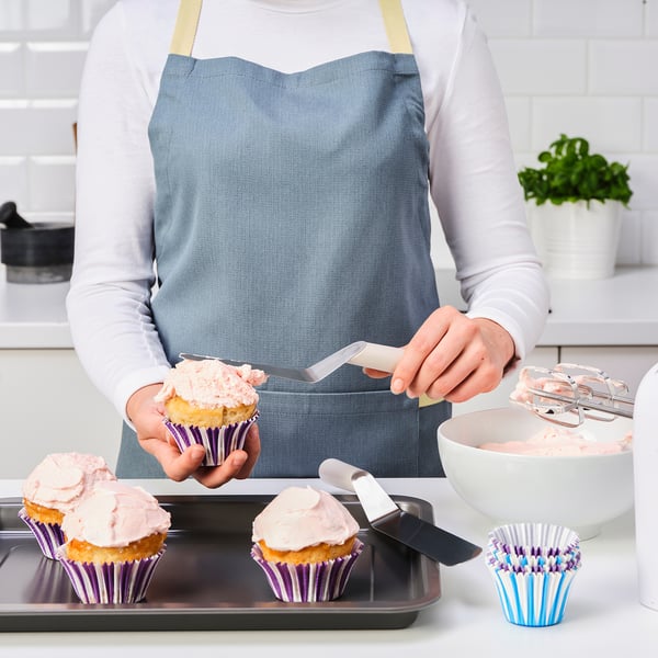 A person is icing cupcakes with a spatula in a kitchen.