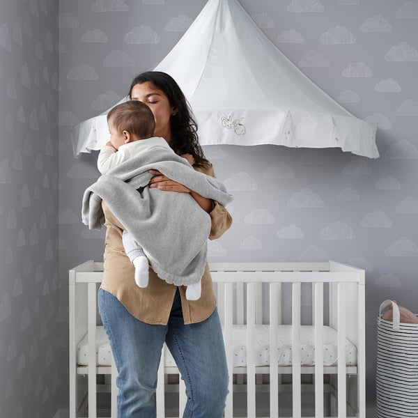 Mother holds baby near crib with soft, sustainable blanket.