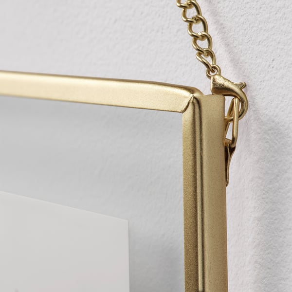 Golden-framed mirror hangs securely from chain on wall, reflecting light and adding elegance.