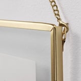 Golden-framed mirror hangs securely from chain on wall, reflecting light and adding elegance.