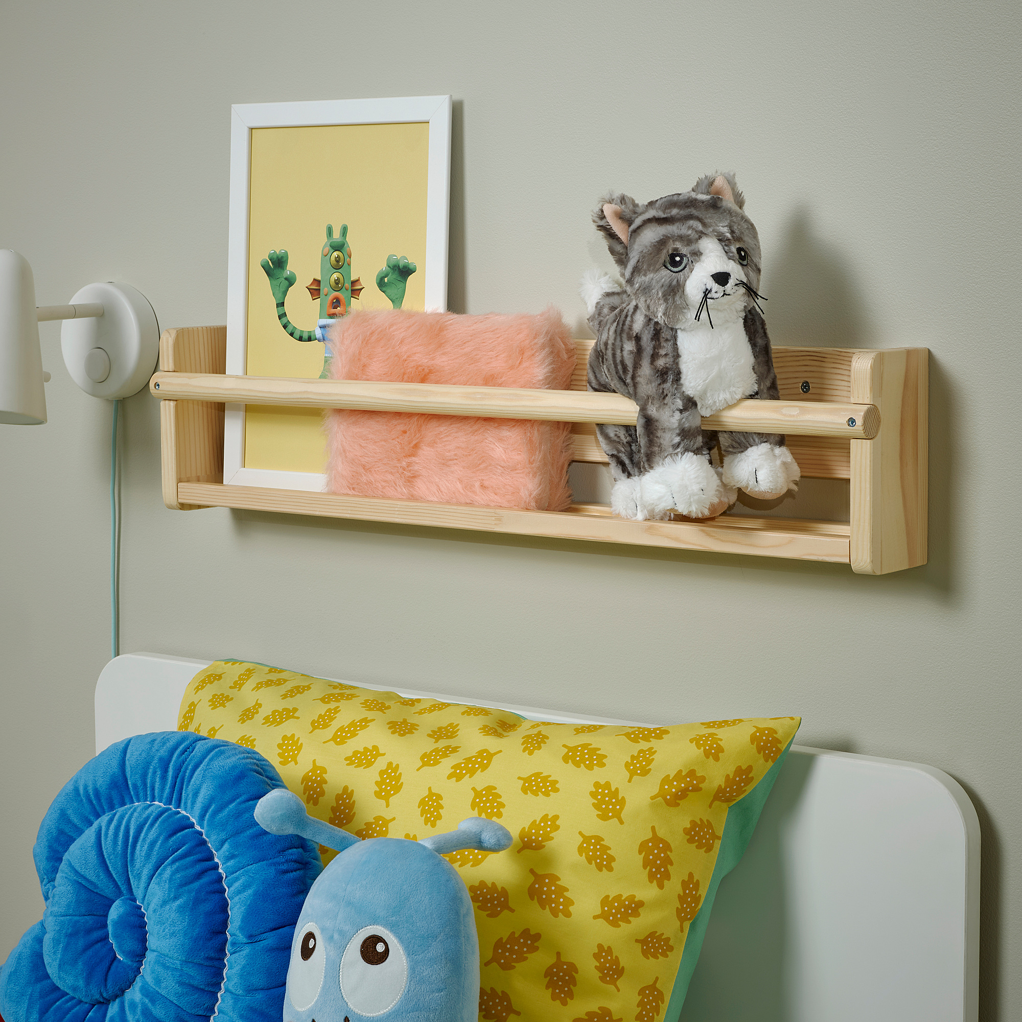 Childs bedroom with wooden shelf, soft blanket, gray cat toy, blue/yellow pillows, elephant-shaped pillow.