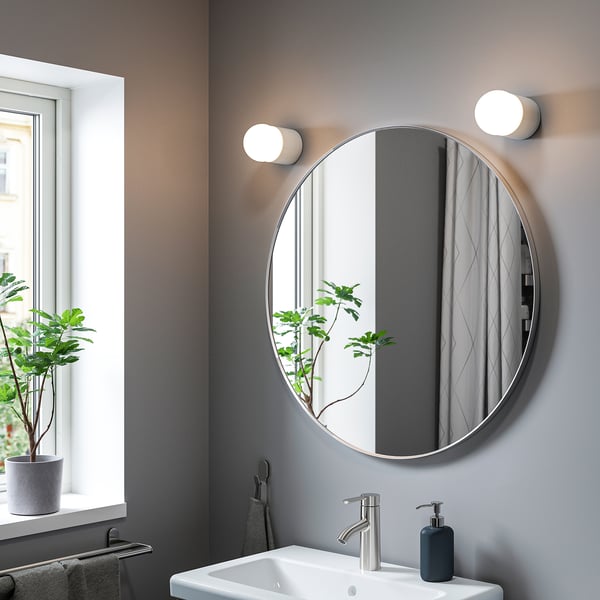 Modern bathroom with large round LINDBYN mirror, silver frame, reflecting plant and sink.