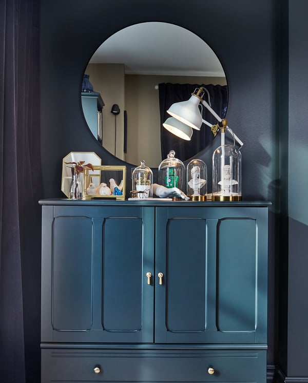 Dark teal LINDBYN mirror cabinet with gold accents and glass displays.