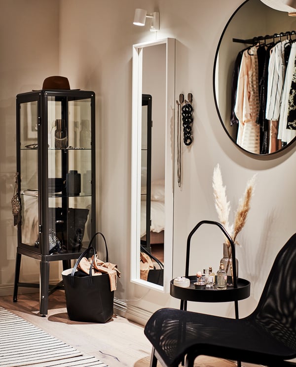 Modern bedroom featuring black LINDBYN mirror with round, elegant frame reflecting a clothes rack and decor items.