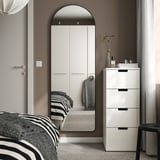 Modern bedroom with LINDBYN arched mirror, large white wardrobe, black framed bed, white drawers, and stool. Mirror and wardrobe dominate the space.
