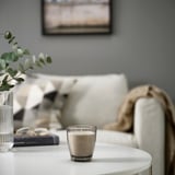 LINDLÖNNSKOG candle beside vase, book, glasses on table near couch with throw.