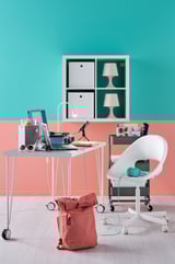 Bright, modern study setup. White desk with laptop, pink lamps, and backpack. Green wall, teal accents.