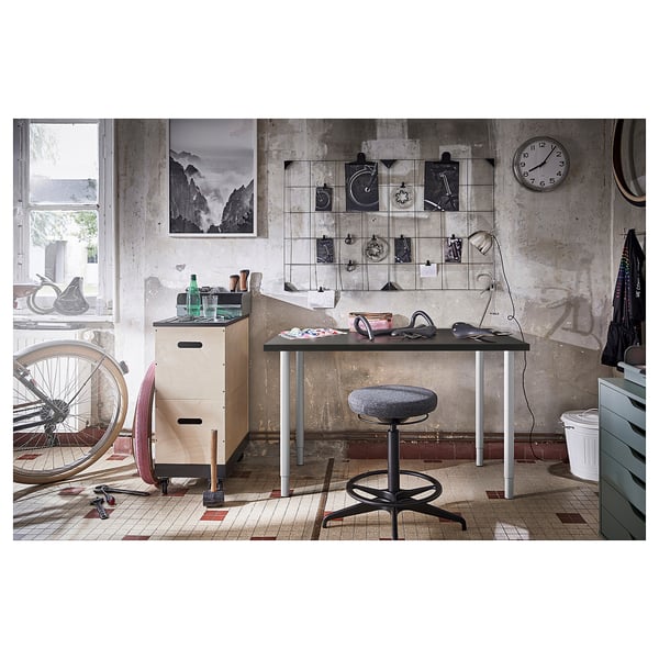Industrial-style workspace with adjustable desk and stool, metal bike.