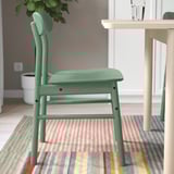 Green wooden chair near dining table on striped rug.