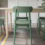 A green LISABO chair with a wooden table. The chair has a stacked design for easy storage, suitable for dining or studying.