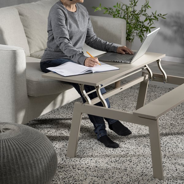 Person sitting on couch using laptop on adjustable table, writing in notebook.