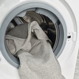 A white washing machine with a grey blanket partially loaded inside. The door is open, revealing the drums interior.