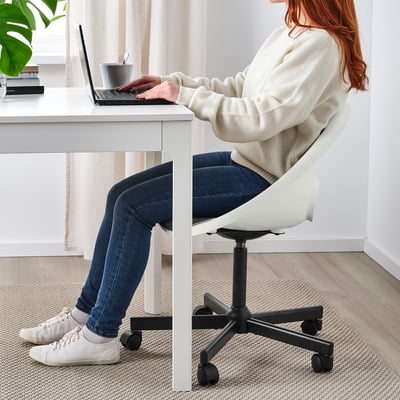 Person sitting in an adjustable, padded office chair with a braking mechanism on wheels, typing on a laptop at a white desk.